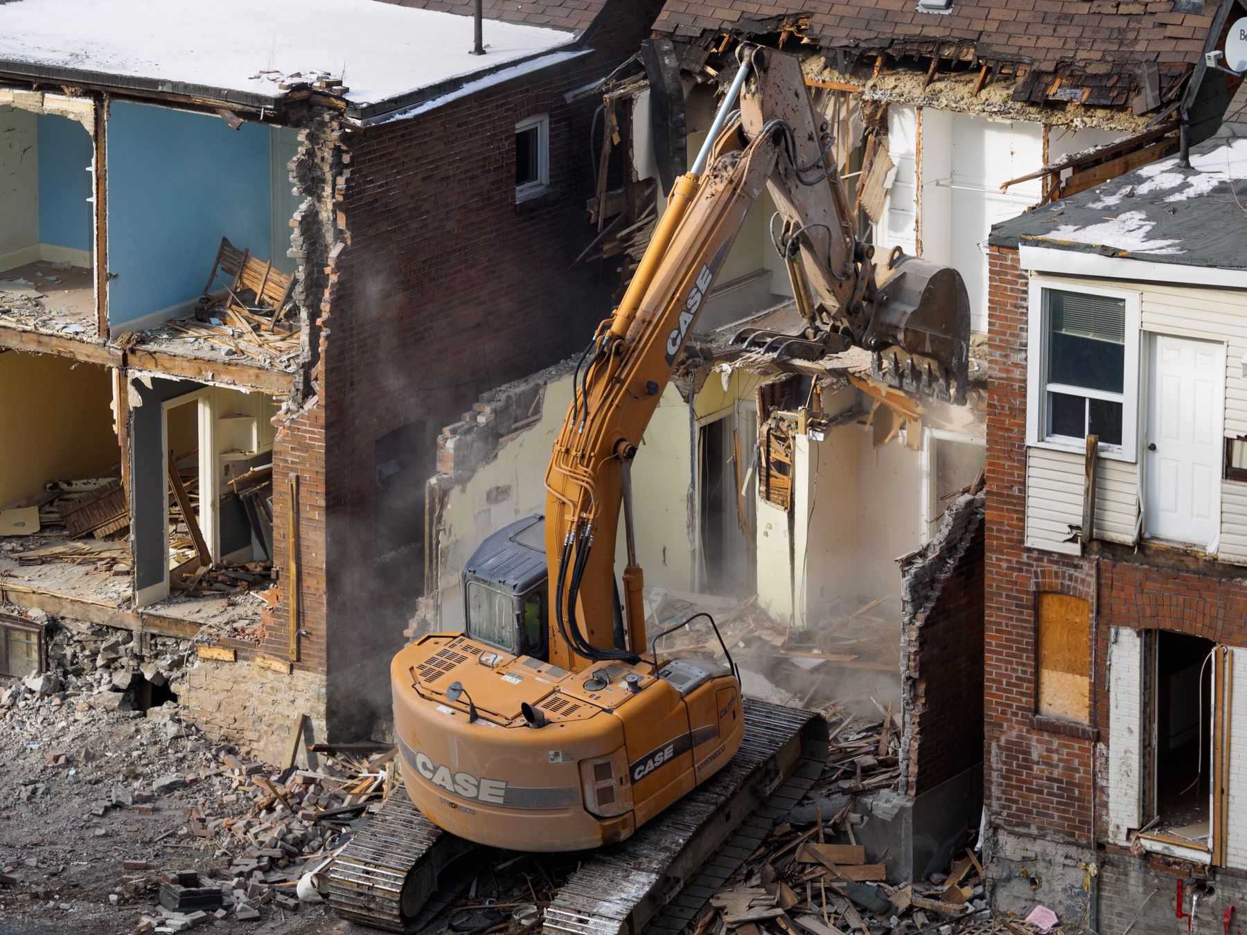 A yellow excavator working inside a partly demolished brick row building, with open rooms visible on each floor.